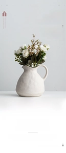 Detail of matte white ceramic pitcher vase with textured finish and artificial roses