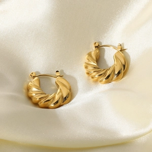 Close-up of golden twisted croissant earrings on elegant beige silk fabric background