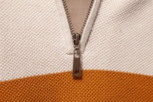 Detailansicht des beigefarbenen Strickpullovers mit orangefarbenem Block und Reißverschluss