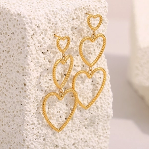 Detailed view of triple tiered gold heart earrings with woven texture on white stone