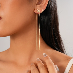 Close-up of elegant gold bow earrings with long tassel snake chains on a model