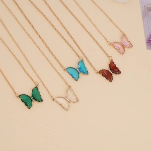 Golden butterfly pendant necklaces in five assorted glass colors on a beige background
