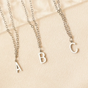 Silver stainless steel A, B, and C letter necklaces with polished finish on warm fabric background