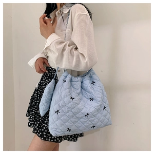 Detail of light blue quilted tote bag with black bow embroidery worn by model