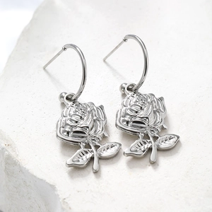 Macro shot of silver rose-shaped earrings with hooks on a minimalist white stone background