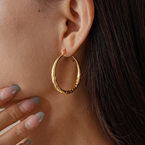 Close-up of gold hoop earrings with geometric diamond-cut texture on a model