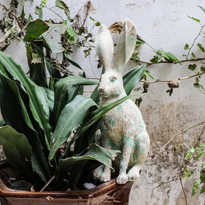 Vintage long-eared rabbit garden statue with distressed green finish in a planter