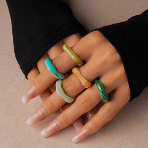 Cinq bagues géométriques en résine aux tons vert et ambre portées par un mannequin