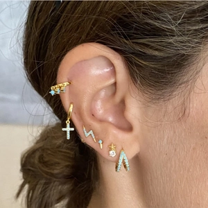 Close-up of golden S925 silver earrings with turquoise and cross charms on ear