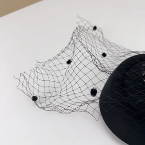 Detailed close-up of a black vintage pillbox hat with mesh veil and polka dot accents
