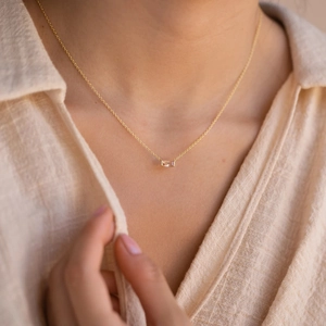 Close-up of a gold minimalist birthstone necklace with a rectangular zircon pendant