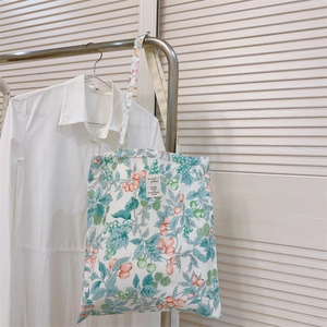 Detail of floral canvas tote bag with orange berry print hanging on a metal hanger
