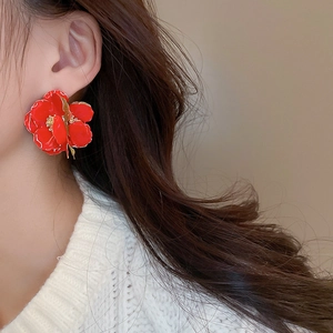 Elegant 3D red flower stud earrings with gold trim worn by a model in a close-up shot
