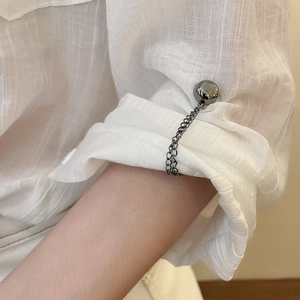 Close-up of silver metal chain magnetic buckle holding a white textured shirt sleeve