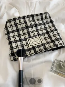 Detail of plaid tweed makeup bag with zipper and Pleasant Time label on bedsheet