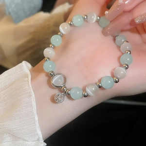 Detail of beaded bracelet with green cat-eye stones and silver hollow charm on wrist