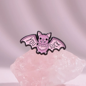 Cute pink bat enamel pin with You Suck text shown on a pink decorative crystal base