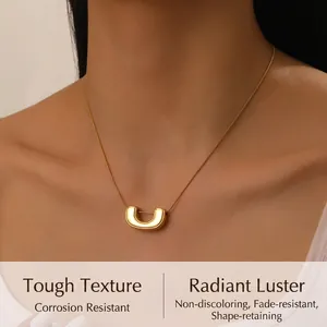Close-up of a gold U-shaped pendant on a snake chain worn by a female model