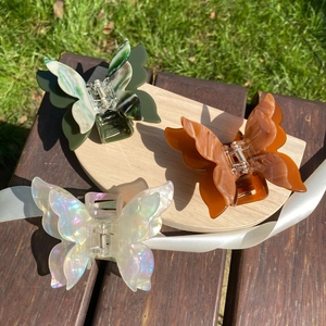 Close-up of three iridescent butterfly hair claws on a wooden tray with white ribbons