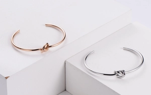 Detail view of knot design on minimalist open bangles in rose gold and silver finishes