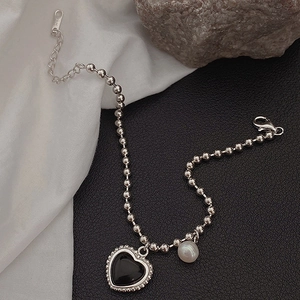 Macro detail of S925 silver beaded chain with black heart pendant and elegant pearl accent
