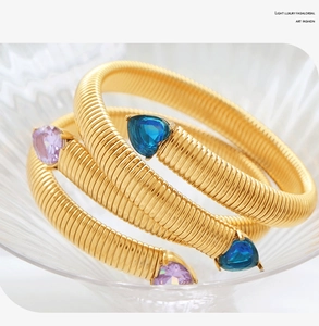 Detail of gold snake-bone elastic bracelet with heart-shaped blue and purple gemstones
