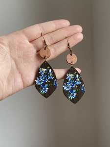 Detailed view of handmade teardrop wood earrings with blue floral pattern and metal hook