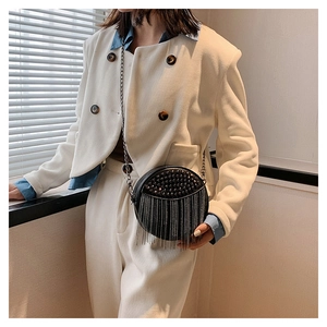 Detail of round black crossbody bag with metal tassels and silver chain strap
