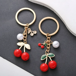 Red cherry pearl keychains with gold metal leaf and green enamel accents on dark gray base