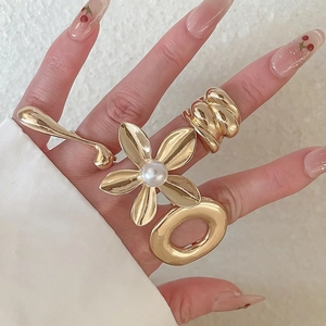 Detail of four gold-finish metal rings featuring a pearl flower and teardrop design