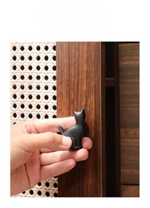 Close-up of black cast iron cat-shaped cabinet handle installed on dark wood drawer
