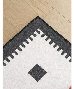 Close-up of chenille rug texture with grey and beige geometric patterns and stitched edges