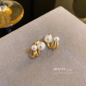 Elegant C-shaped gold metal earrings with double white pearls on a velvet display stand