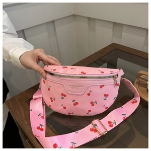 Pink cherry print crossbody bag with wide shoulder strap displayed on a glass table