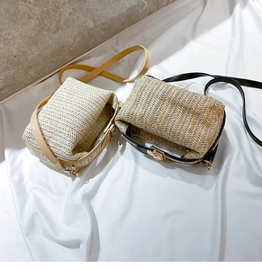 Detail of woven straw shoulder bags with beige and black straps on white fabric