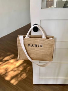 Detail of woven straw tote bag with Paris embroidery hanging on a white wooden door