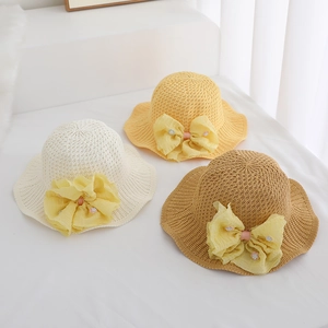 Detailed overhead view of woven sun hats in beige and yellow with large ribbon bows
