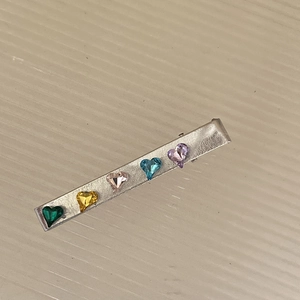 Dettaglio di un lungo fermaglio d'argento con cinque cristalli colorati a forma di cuore