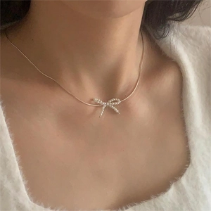 Elegant gold bow necklace with white pearls on a snake chain, worn by a model