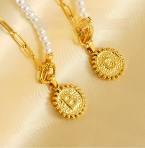 Close-up of a gold-plated stainless steel necklace with pearls and an engraved B-G pendant