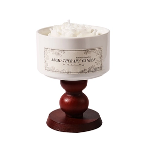 White flower-shaped scented candle in a white ceramic cup with a carved wooden base