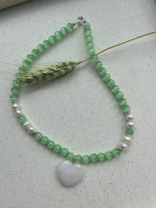 Macro detail of icy blue cat eye beads and white heart pendant on a textured fabric