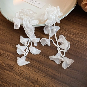 Detail view of elegant white chiffon flower earrings with long beaded tassels on wood