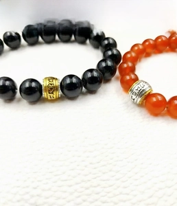Close-up of black and red beads with engraved mantra barrel charms on white leather