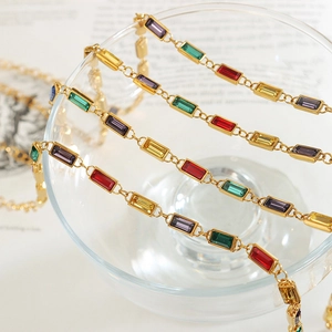 Vintage gold necklaces with vibrant rectangular crystals draped over a glass
