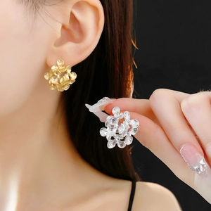 Close-up of matte gold and silver flower earrings worn by a model against dark background