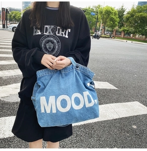 Detail of blue denim tote bag with white 'MOOD' lettering in an outdoor street setting