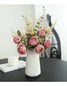Close-up of pink artificial roses and greenery in a white ceramic vase for home decor