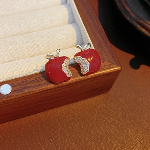 Detailed close-up of red enamel apple stud earrings with crystals on a jewelry box