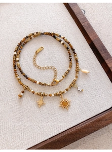 Detail of bohemian tiger eye beaded necklace with gold sun and star charms on fabric